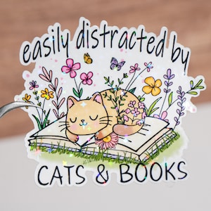 May include: A sticker with a cat sleeping on a book surrounded by flowers and butterflies. The text reads "easily distracted by cats & books".
