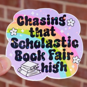 Puede incluir: Una pegatina holográfica con un diseño de arcoíris y el texto "Chasing that Scholastic Book Fair high".
