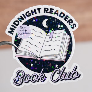 May include: A holographic sticker with a black background and a white open book with a purple bookmark. The sticker says "Midnight Readers Book Club" in a white cursive font with a crescent moon and stars. A small purple circle with the text "One more chapter" is in the top left corner.