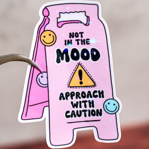 Könnte beinhalten: Rosa-gelber Warnschild-Aufkleber mit dem Text "Not in the Mood Approach with Caution" und einem gelben Ausrufezeichen in einem Dreieck.