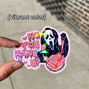 May include: A pink holographic sticker with a cartoon image of Ghostface from the Scream movie franchise holding a pink rotary phone. The sticker says "No You Hang Up" with dripping pink letters and hearts.