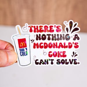 以下が含まれることがあります： マクドナルドのコカ・コーラのカップと「There's Nothing a McDonald's Coke Can't Solve」というフレーズが特徴のホログラフィックステッカー。カップにはマクドナルドのロゴと「Good 'n Cold」の文字が描かれています。