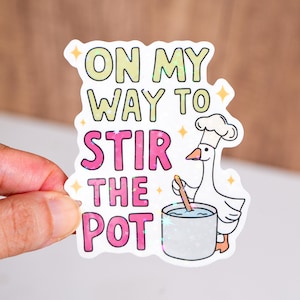 May include: A white sticker with the text "ON MY WAY TO STIR THE POT" in green and pink. A cartoon goose wearing a chef's hat stirs a pot. The sticker has a glittery, holographic effect.