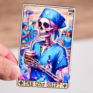 May include: A glittery tarot card with a skeleton wearing a blue surgical scrub and a blue surgical cap. The skeleton is holding a cup of coffee and a straw. The card says "The 12hr Shift" and has a small image of a person in a surgical mask in the corner. The card has a sparkly background.