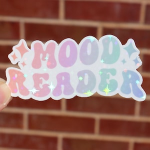 Könnte beinhalten: Ein holografischer Aufkleber mit dem Text "MOOD READER" in einem Regenbogen-Farbschema mit glitzerndem Finish.