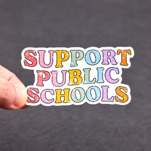 May include: A colourful sticker with the text "SUPPORT PUBLIC SCHOOLS" in a retro font. The words are in different colours, including pink, yellow, blue, and orange, with a sparkly effect.