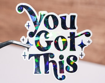 May include: A holographic sticker with the words "You Got This" in a bold, playful font. The sticker has a white border with small cross and star accents. The text and accents have a colorful, iridescent finish.