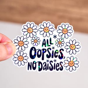 May include: A white sticker with a holographic finish featuring a daisy design and the text "All * Oops*ies, No Daisies".