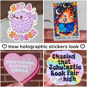 May include: Four holographic stickers with different designs. The first sticker is a purple pufferfish with the text "Not a Hugger". The second sticker is a skeleton in a dumpster fire with the text "The Emotional Dumpster Fire". The third sticker is a pink heart with the text "Emotional Support Kindle". The fourth sticker is a rainbow with the text "Chasing that Scholastic Book Fair High".