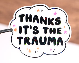 May include: White sticker with a black cloud shape and the text "Thanks it's the trauma" in black with a glittery finish. The sticker is decorated with small pink and orange stars.