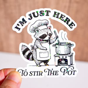 May include: A sticker featuring a cartoon raccoon chef stirring a pot on a stove. The text "I'm just here" arches above the raccoon, and "To stir the pot" is below. The sticker has a holographic effect.