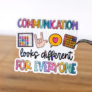 以下が含まれることがあります： 「COMMUNICATION」と「looks different FOR EVERYONE」の文字が入ったホログラフィックステッカー。タブレット、手の「愛してる」サイン、ハートの吹き出し、コミュニケーションボードのイラストが特徴です。