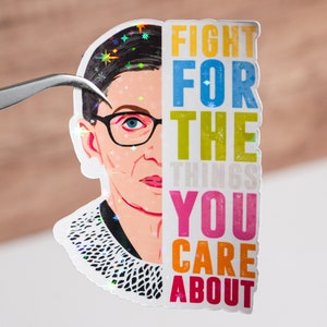 May include: A sticker featuring a colorful illustration of Ruth Bader Ginsburg with the text "Fight for the things you care about".