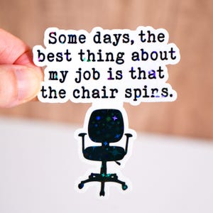 May include: A holographic sticker with the text "Some days, the best thing about my job is that the chair spins." The sticker features a black office chair graphic with a starry design.