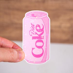 May include: Pink can with a white outline and a sparkling effect. The can has the text "Diet Coke" in pink lettering.