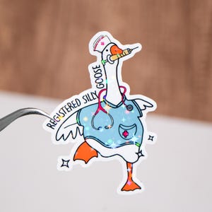 May include: A holographic sticker of a cartoon goose wearing a blue scrubs uniform with a red stethoscope and a nurse's hat. The goose is holding a syringe and the text "Registered Silly Goose" is written around the goose.