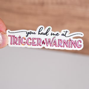 May include: White sticker with pink and black text that reads "You had me at trigger warning".