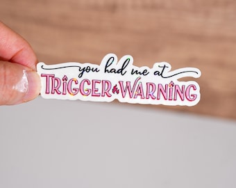 Może przedstawiać: Biała naklejka z różowym i czarnym tekstem, który brzmi "You had me at trigger warning".