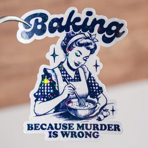 May include: A white sticker with a blue and silver holographic finish. It features a cartoon illustration of a woman baking with the text "Baking because murder is wrong."