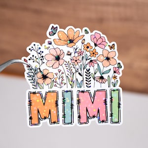 May include: A sticker featuring a floral design and the word "MIMI" in a rainbow of colours. The flowers are pink, orange, and yellow with green stems and leaves.