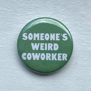May include: A green button with the white text "SOMEONE'S WEIRD COWORKER". The button is circular and likely intended as a novelty item. The background is a light, textured surface. A fun item for the workplace.