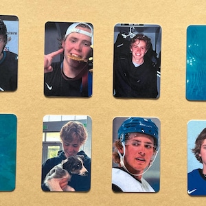 Può includere: Una collezione di otto carte collezionabili rettangolari con varie fotografie di una persona giovane. Le immagini includono ritratti con attrezzatura da hockey, una persona che tiene una medaglia d'oro, una persona con un cagnolino e due carte color ottanio.