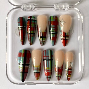 Peut inclure: Un ensemble de dix faux ongles avec un motif à carreaux. Les ongles sont dans un étui en plastique transparent. Les ongles sont longs et pointus, et ils ont un motif à carreaux rouge, bleu et vert. Certains ongles ont un accent étoile argenté.