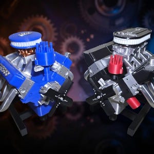 May include: Two model car engines, one blue and one black, are displayed. The blue engine has silver exhaust pipes and a white air filter. The black engine has red accents. Both are mounted on black stands, showcasing intricate details.