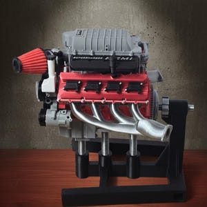 May include: A detailed scale model of a supercharged HEMI engine featuring a grey engine block, bright red valve covers, silver exhaust headers, and a prominent red conical air filter. The engine is mounted on a black stand with adjustable supports.