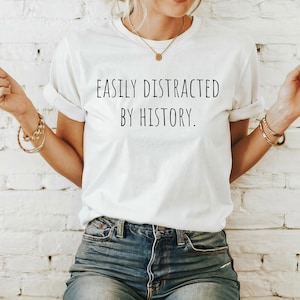May include: White t-shirt with the text "EASILY DISTRACTED BY HISTORY." printed in black.