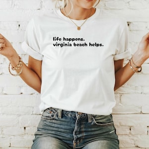 May include: White t-shirt with black text that reads "life happens. virginia beach helps."