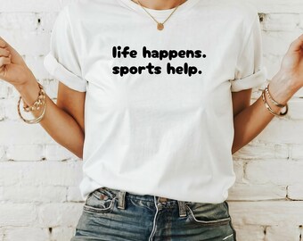May include: White t-shirt with black text that reads "life happens. sports help."