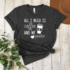 Op de afbeelding: Donkergrijs t-shirt met de witte tekst "ALL I NEED IS coffee AND MY pointer". Een koffiekopje met een pootafdruk en een hart zijn ook afgebeeld. Het t-shirt is aan de onderkant geknoopt.