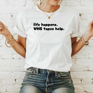 May include: White t-shirt with black text that reads "life happens. VHS tapes help."
