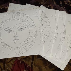 May include: A set of six blank white paper sheets with a black line drawing of a sun and moon with faces on one sheet. The drawing is in a circle with a decorative border.