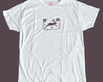 May include: White t-shirt with a black and white illustration of a rabbit jumping through a heart-shaped frame with floral accents.
