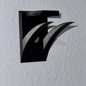 May include: A black plastic wall mount with a curved design. The mount has a small hole in the center.