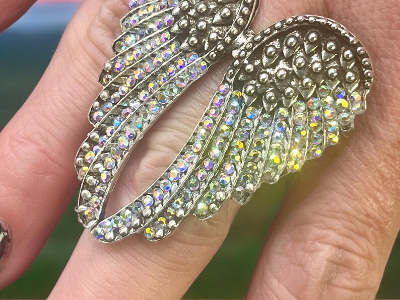 Size 8 Angel Wing Statement Ring with crystal rhinestones. Made of alloy, measures 3x4x2 cm, 13 oz. Trendy and stylish, perfect for daily wear or special occasions. A must-have accessory for those who love bold, unique jewelry.