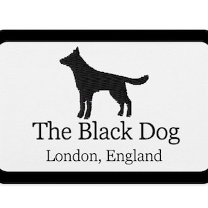 May include: A rectangular patch with a black border features a black silhouette of a dog above the text "The Black Dog" and "London, England" in a serif font. The background is white.