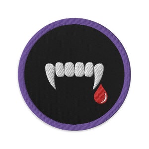 May include: Circular embroidered patch with a black background, featuring white fangs and a red blood drop. The patch has a purple border. Suitable for Halloween or vampire-themed clothing and accessories.