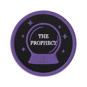 May include: Embroidered patch with a black background and a purple border. The patch features a crystal ball design with the words "THE PROPHECY" in white. Four purple stars surround the crystal ball, creating a mystical theme.