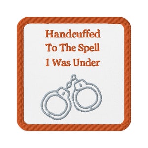 May include: Square patch with an orange border and white center. The text "Handcuffed To The Spell I Was Under" is in orange. Below the text is a gray illustration of handcuffs.
