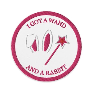 May include: Embroidered patch with a white centre and a fuchsia border. The patch features the text "I GOT A WAND AND A RABBIT" in fuchsia, along with a wand and rabbit ears.