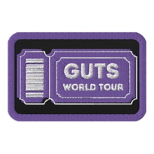 May include: Embroidered patch in the shape of a ticket, featuring the words "GUTS WORLD TOUR" in white thread on a purple background. The patch has a black border and a ticket-style design on the left side.