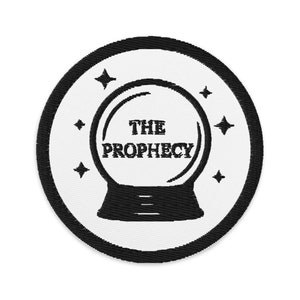 May include: Embroidered patch featuring a crystal ball design with the text "THE PROPHECY". The patch is circular, with a black border and a white background. Four black star shapes surround the crystal ball.