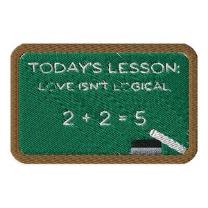 May include: Embroidered patch depicting a green chalkboard with white text: "TODAY'S LESSON: LOVE ISN'T LOGICAL" and "2 + 2 = 5". A chalk stick is at the bottom right. The patch has a brown border.