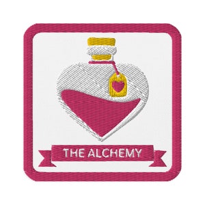 May include: Embroidered patch featuring a heart-shaped potion bottle filled with pink liquid. The bottle has a yellow stopper and a tag with a heart. The patch is framed in a pink border, with the text "THE ALCHEMY" on a banner.