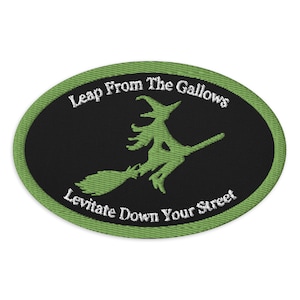 May include: An oval patch with a black center and a green border. The patch features a green witch on a broomstick with the text "Leap From The Gallows" above and "Levitate Down Your Street" below. The design is embroidered.