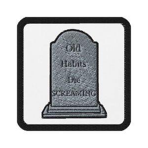 May include: Embroidered patch featuring a gray tombstone design with the words "Old Habits Die SCREAMING" in capital letters. The patch has a white background and a black border, suitable for clothing or accessories.