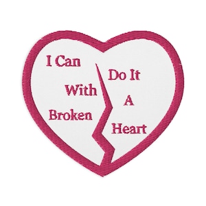 May include: Embroidered heart-shaped patch with a broken design. The patch features the text "I Can With Broken Heart Do It A" in a pink color, outlined by a pink border. The background is white.